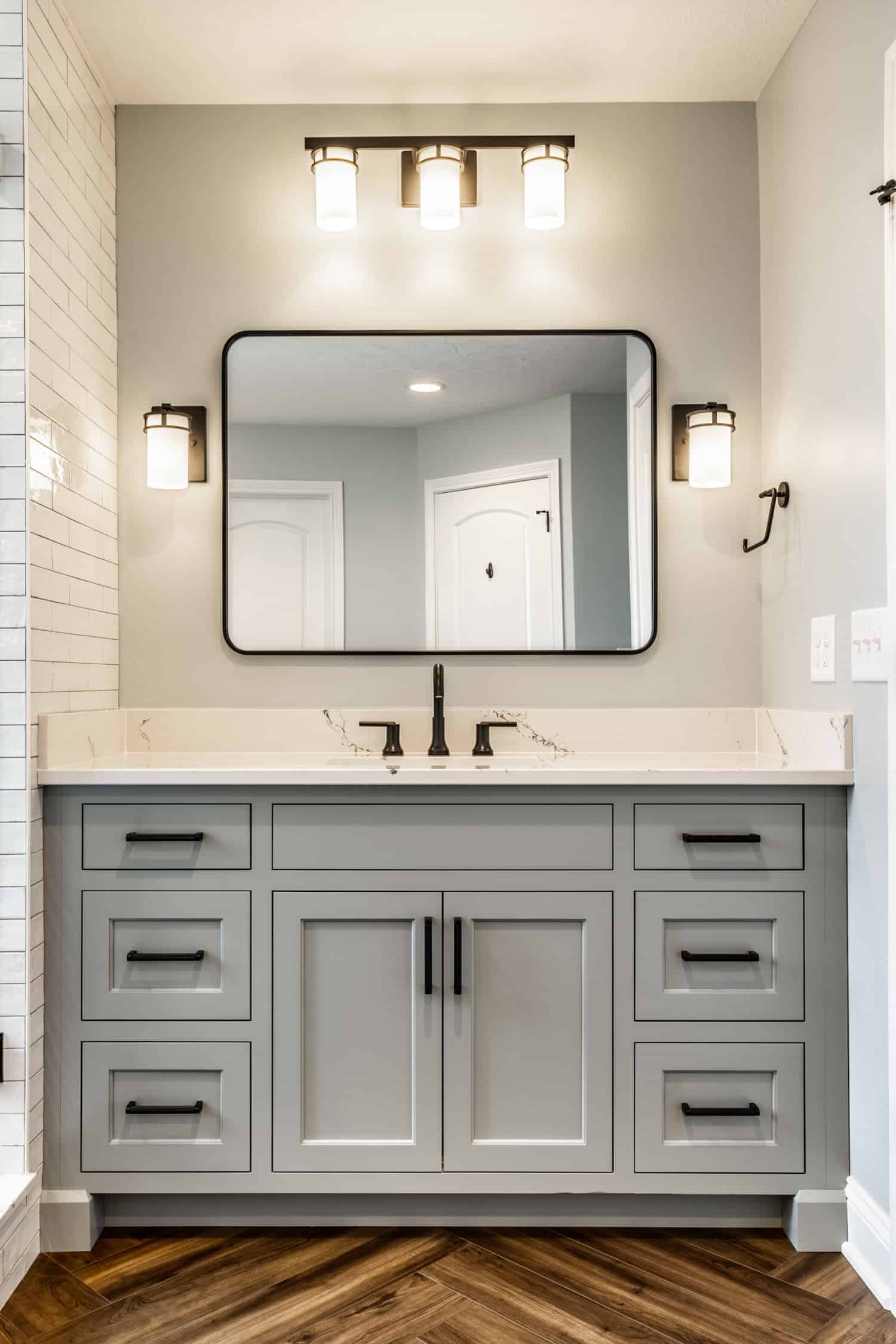 Nicholas Design Build | A bathroom with a gray vanity and mirrors, decorated in black accents.