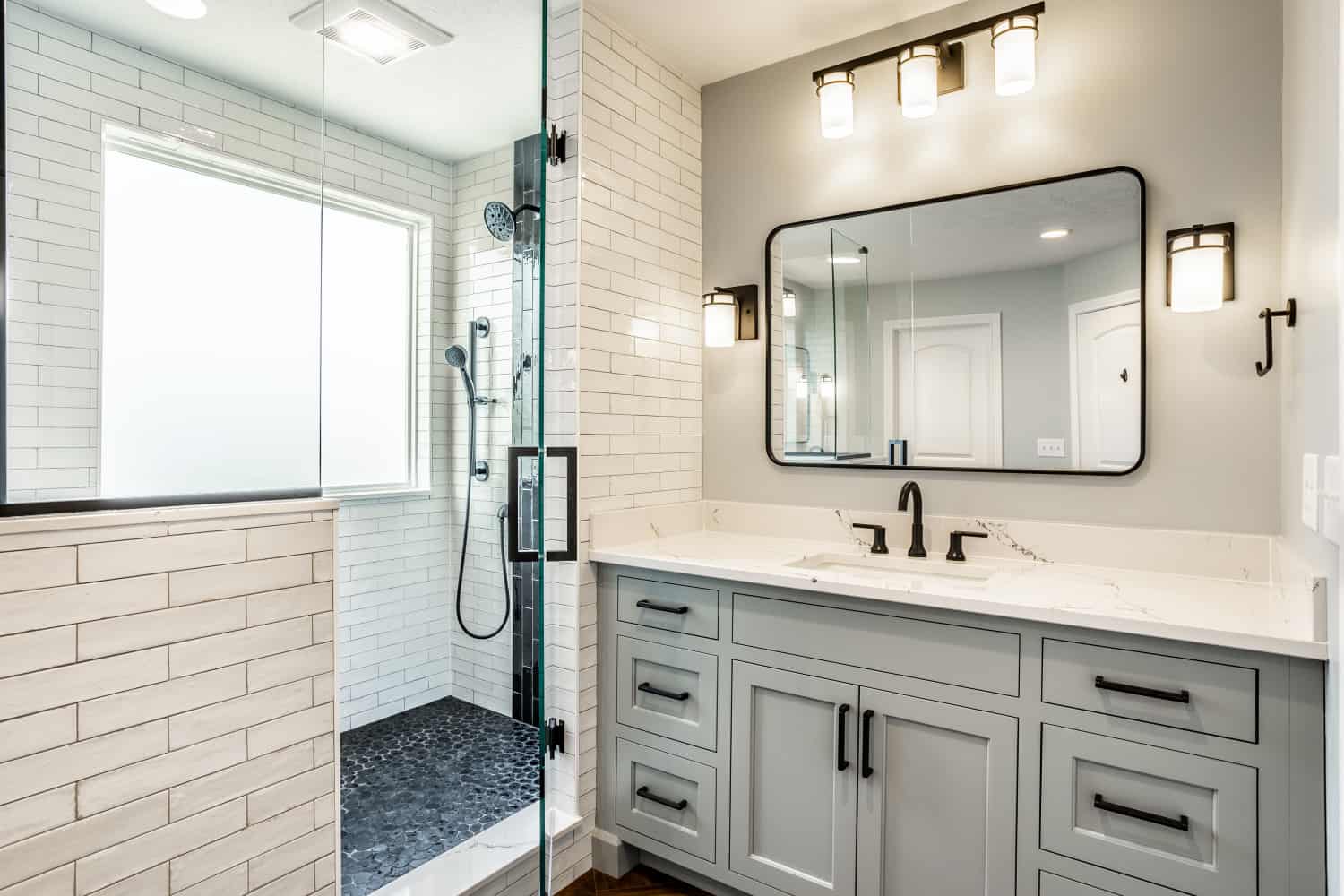 Nicholas Design Build | A bathroom with white cabinets and a glass shower in black and blue.