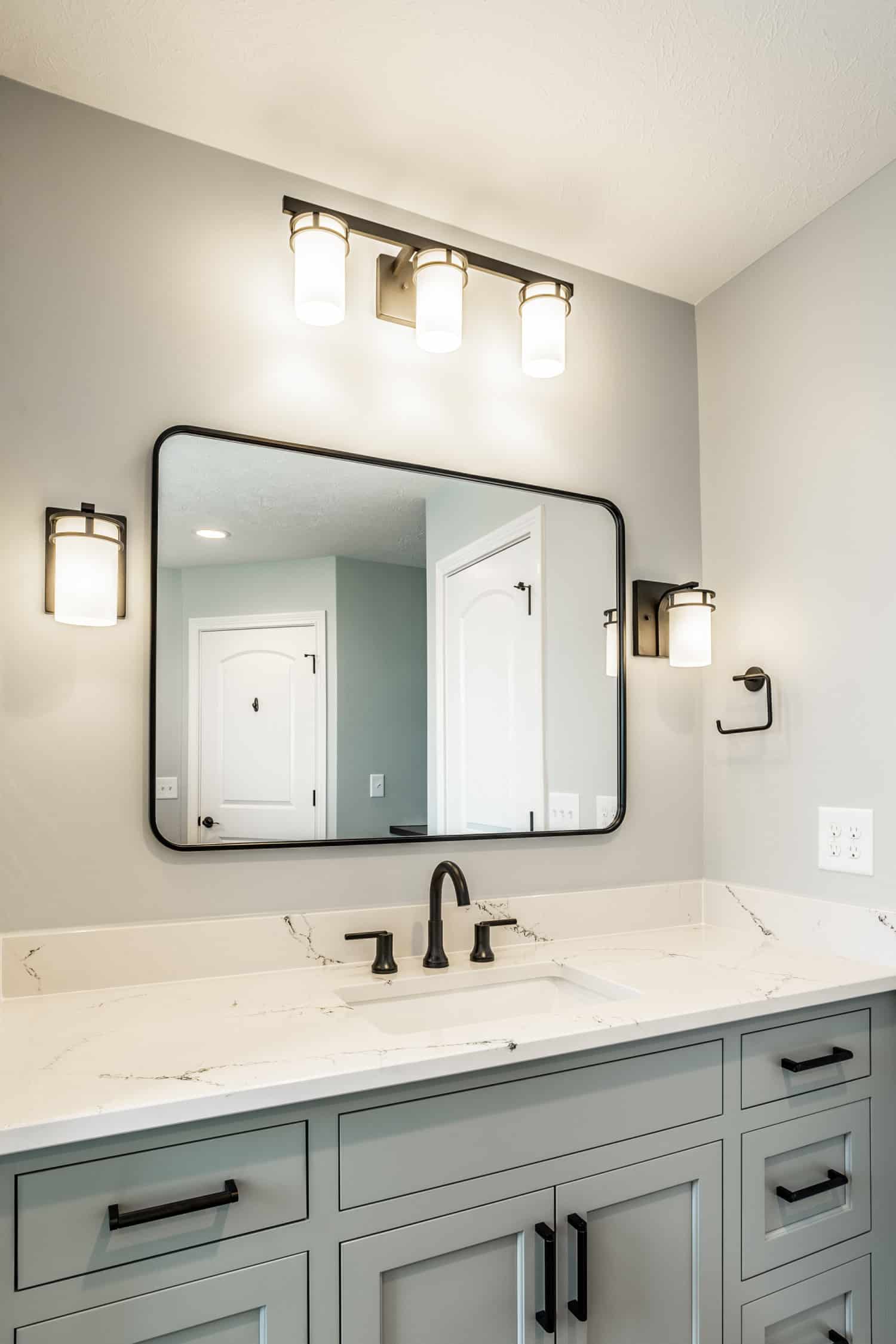 Nicholas Design Build | A bathroom with gray cabinets and a mirror, featuring black accents.