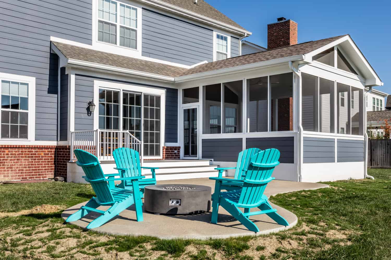 Nicholas Design Build | A remodeled patio with blue chairs and a fire pit in front of a house.