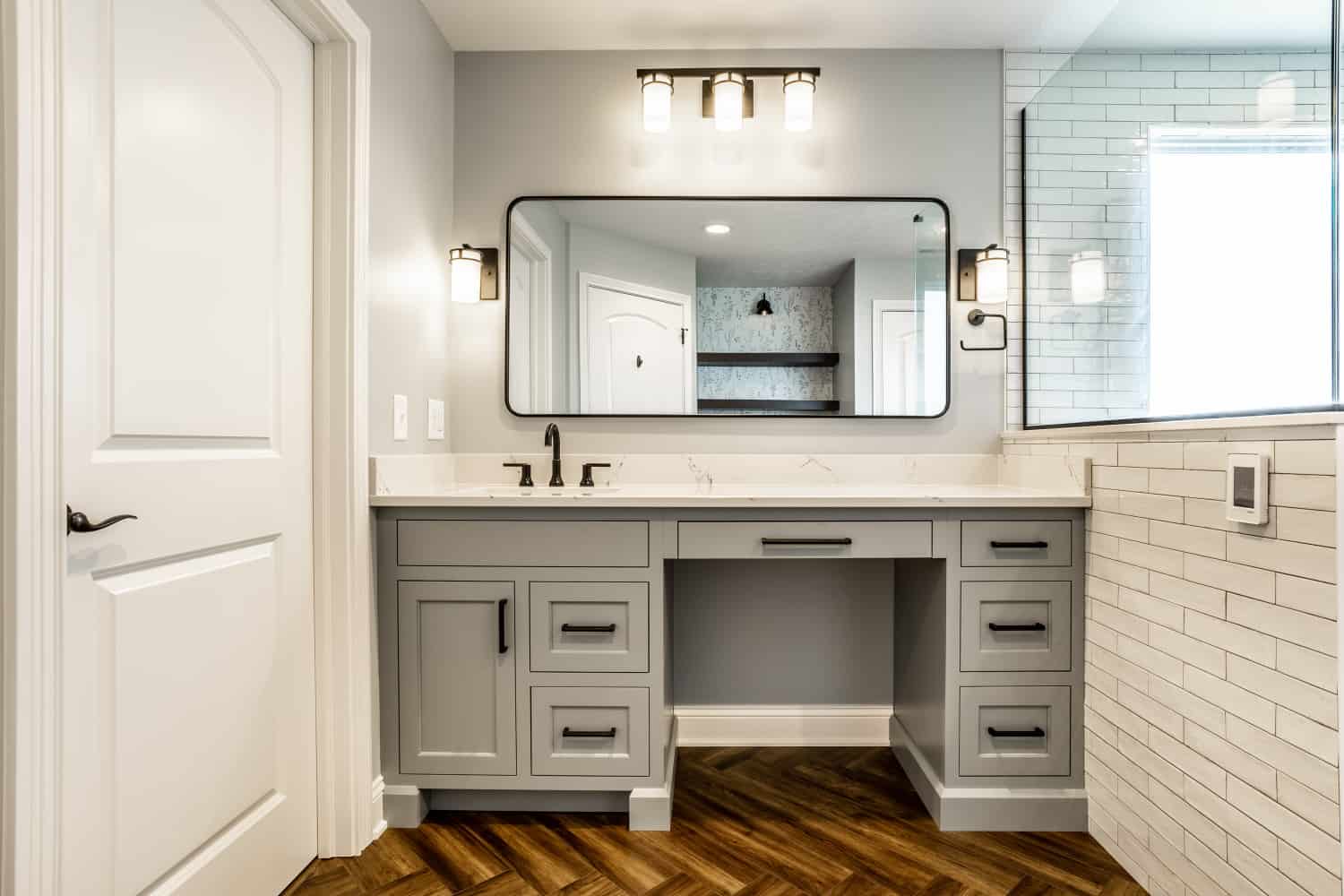 Nicholas Design Build | A bathroom with a white vanity and wood floors, featuring black accents.