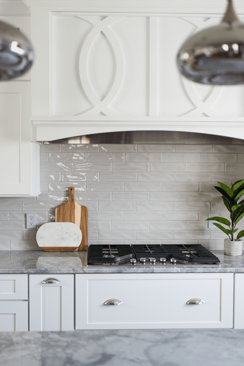 Nicholas Design Build | A white kitchen with a marble backsplash and a potted plant.