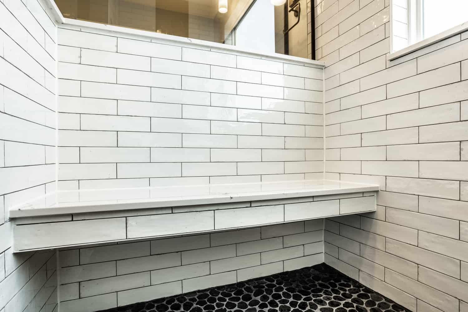 Nicholas Design Build | A black and white tiled shower with a bench in a Black Bathroom.