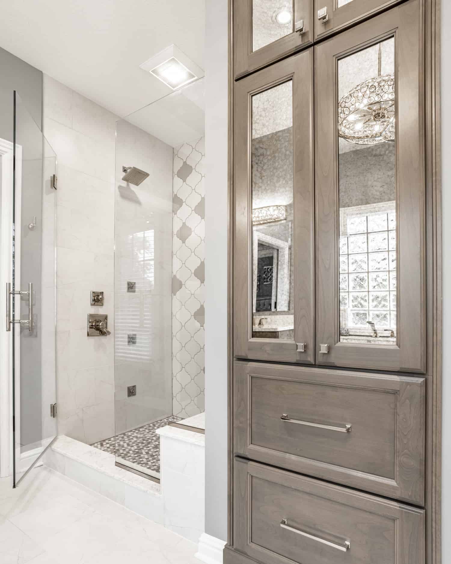 Nicholas Design Build | A bathroom with gray cabinets and a glass shower door featuring a barn door-style entry.