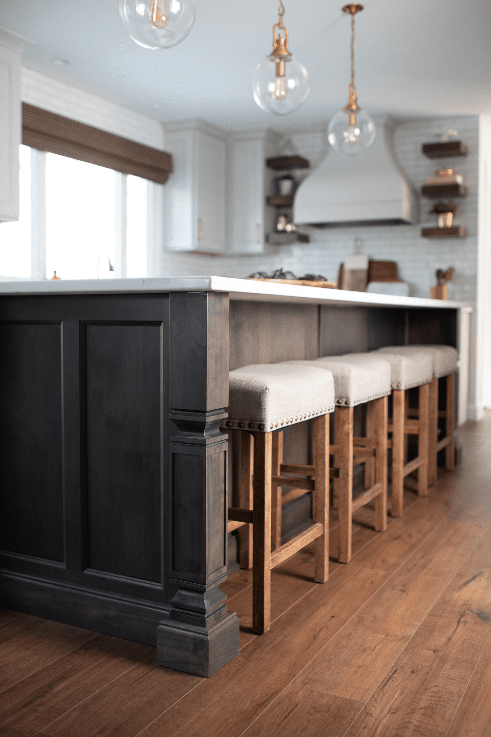 Nicholas Design Build | A kitchen with a black island, wooden stools, and neutral accents.