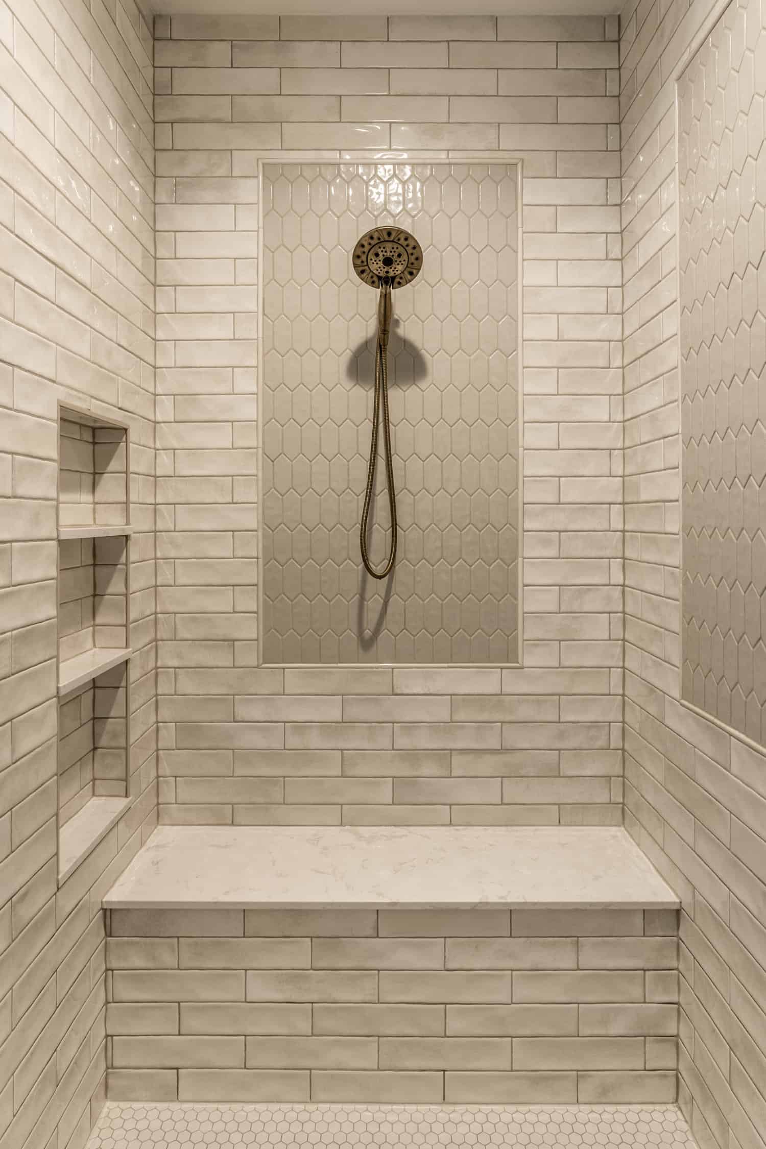 Nicholas Design Build | A modern white tiled shower with a bench and shower head, featuring sleek brushed gold accents.