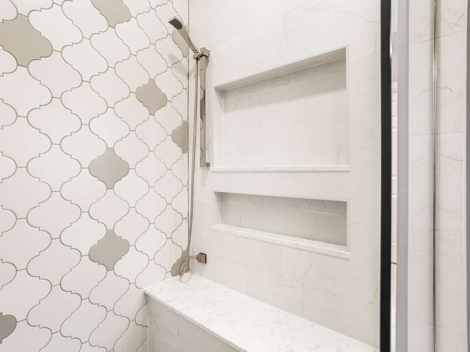 Nicholas Design Build | A white and gray tiled shower with a shelf, perfect for a barn door bathroom.