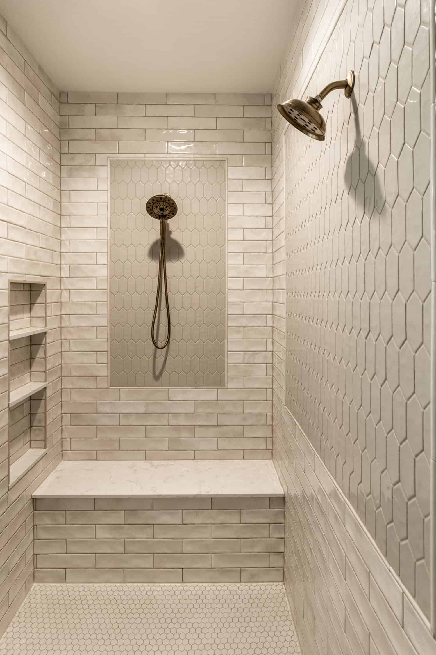 Nicholas Design Build | A modern white tiled shower with a bench and brushed gold shower head.