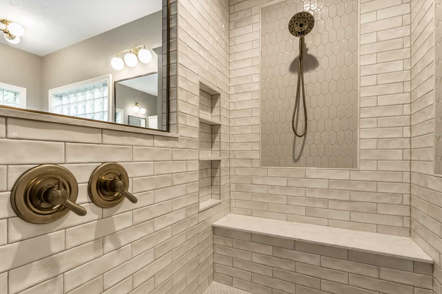 Nicholas Design Build | A modern bathroom with white tile and a brushed gold shower head.