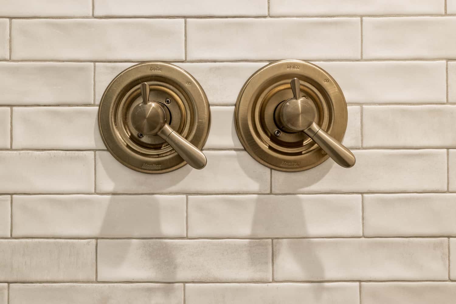Nicholas Design Build | Two modern brass faucets on a white tiled wall.