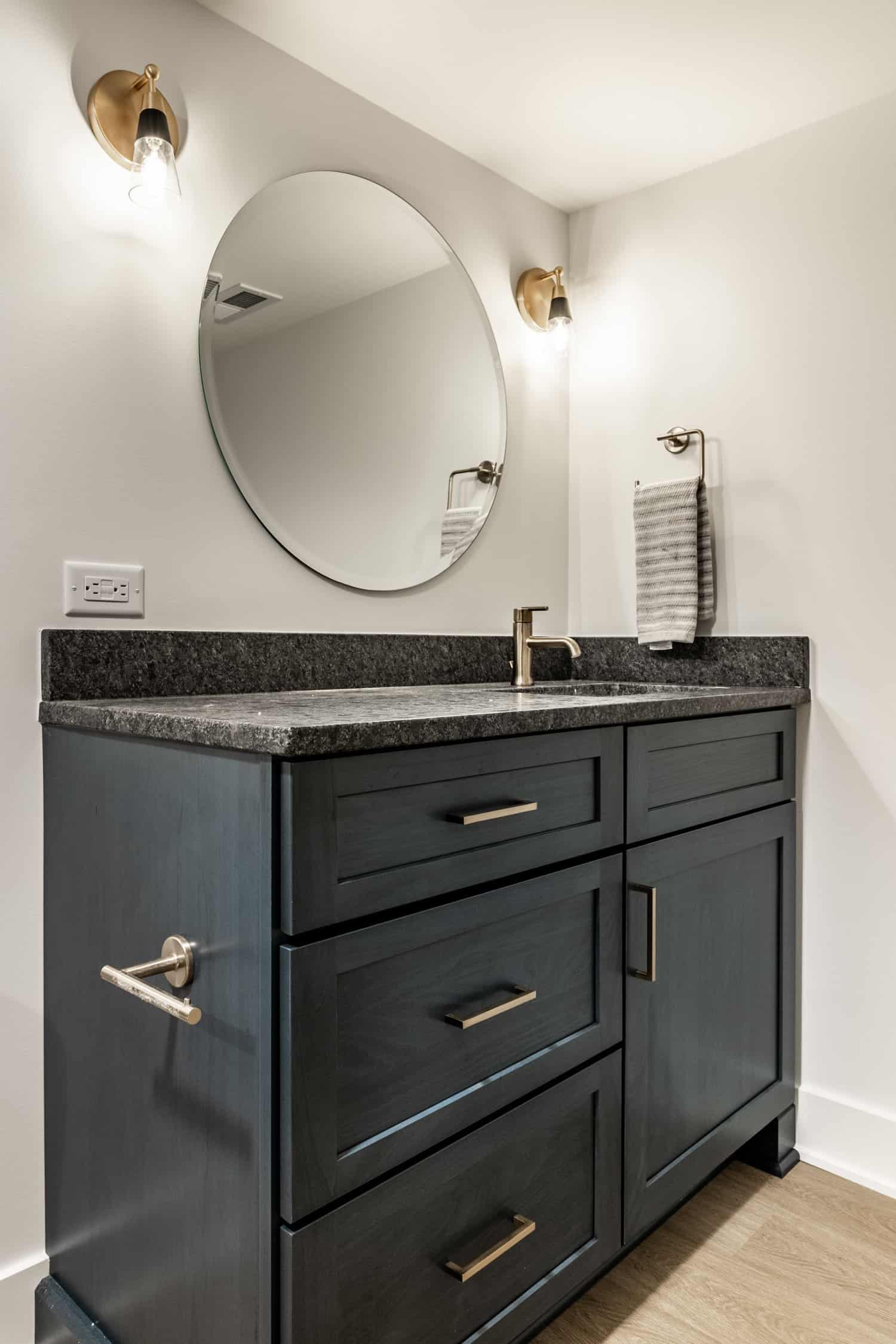 Nicholas Design Build | Remodel a bathroom with black cabinets and a round mirror.
