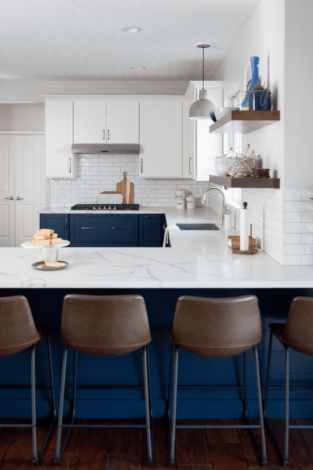 Nicholas Design Build | A white kitchen with blue cabinets and brown stools.