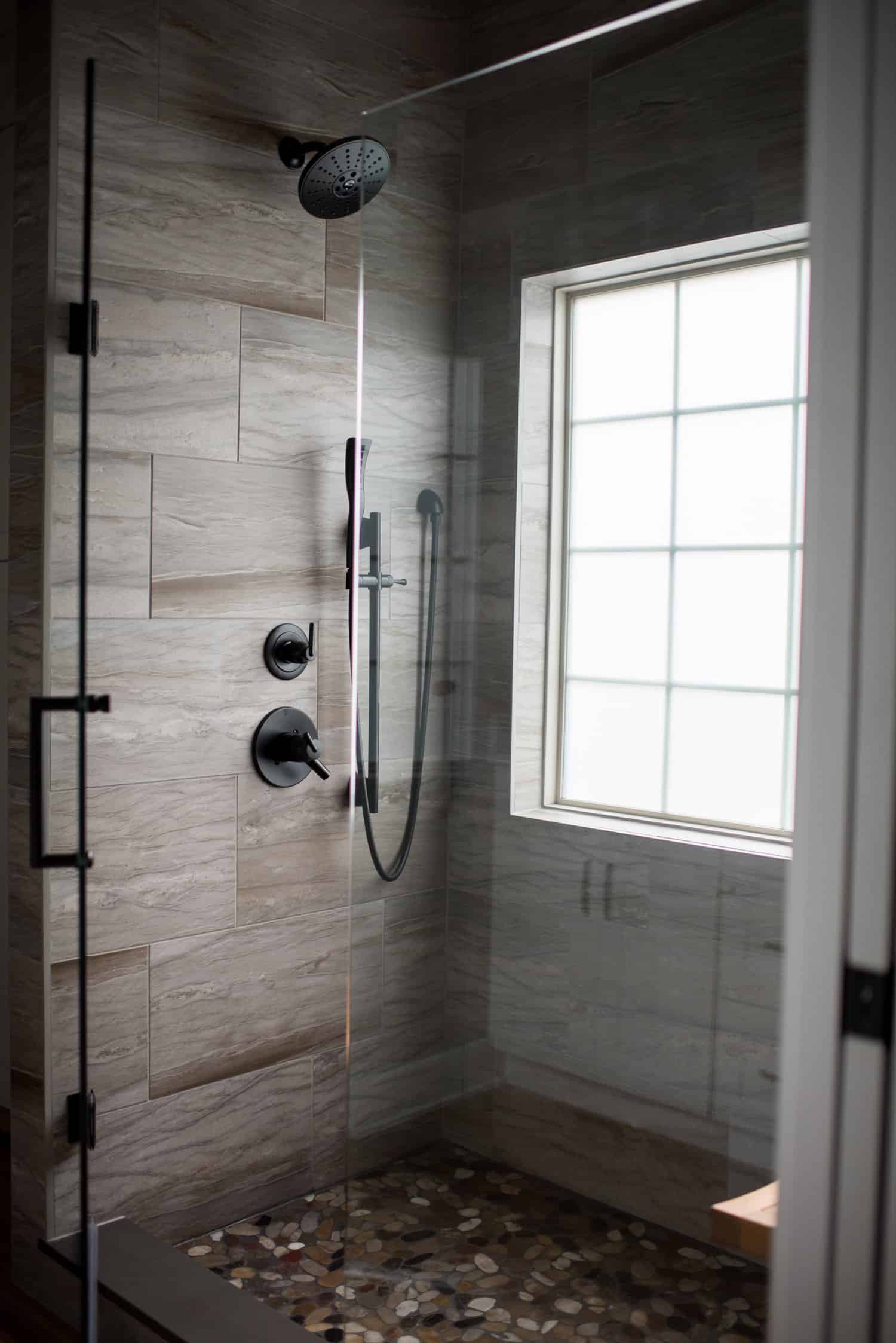 Nicholas Design Build | A modern bathroom with a glass shower door and a window.