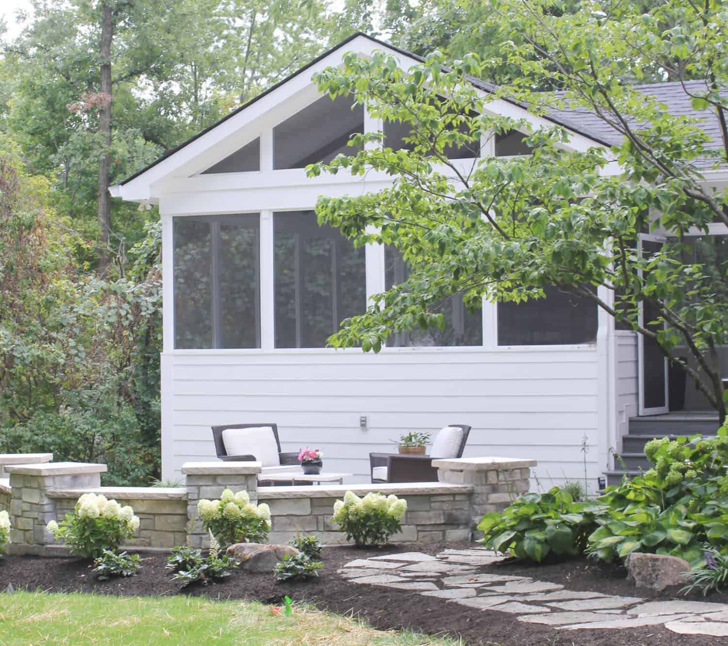 Nicholas Design Build | A small backyard with a white house and a stone patio.