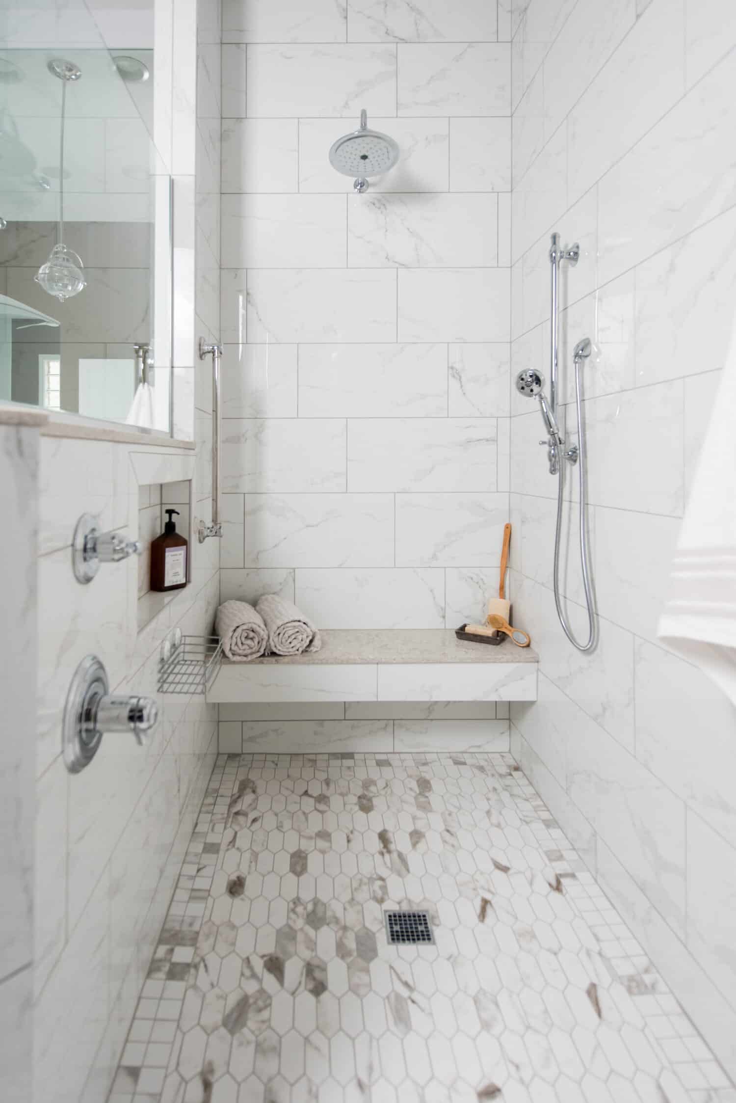 Nicholas Design Build | An oasis-like white tiled shower with a bench and shower head.