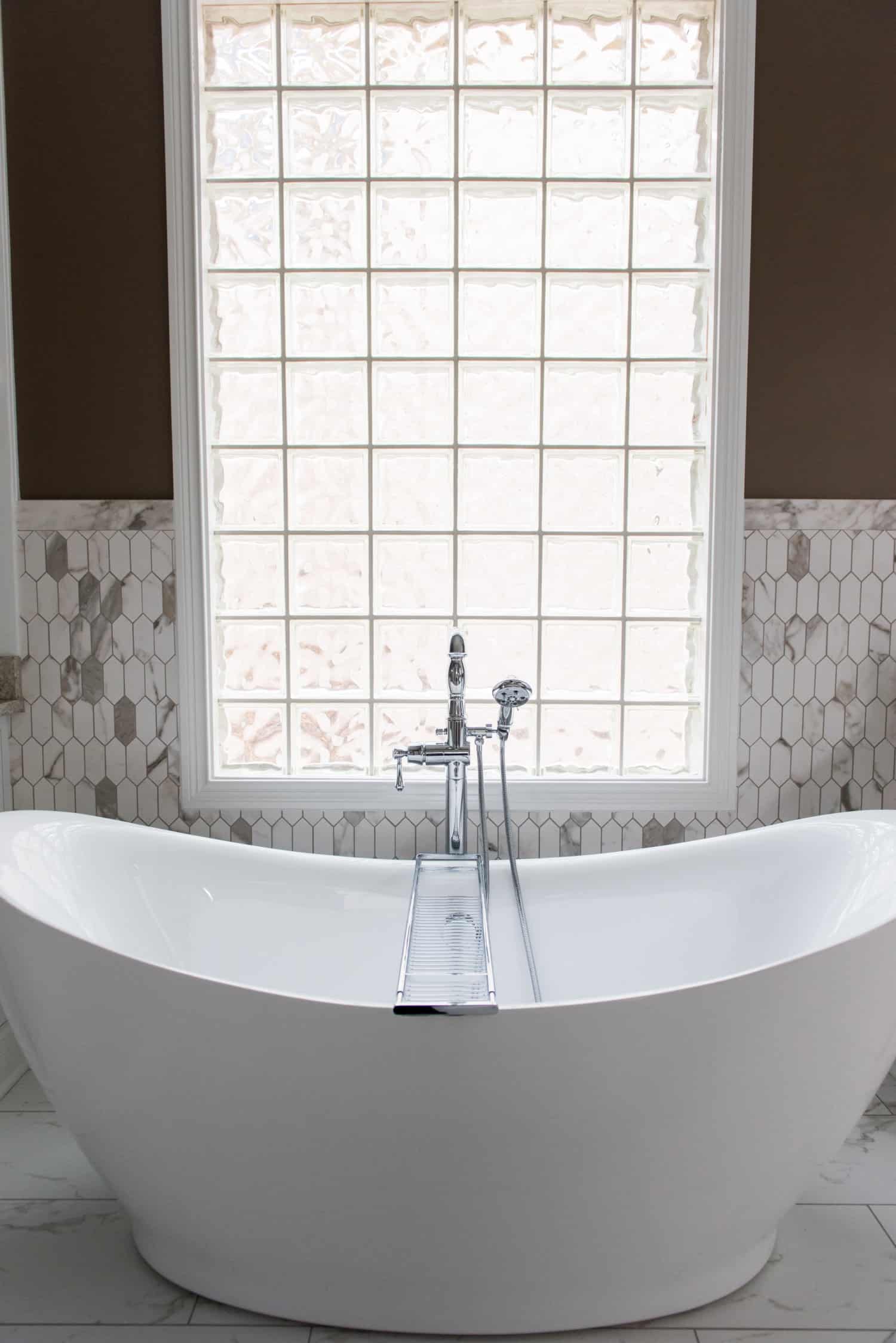 Nicholas Design Build | A white bathtub in a tranquil bathroom oasis with brown tile and a window.