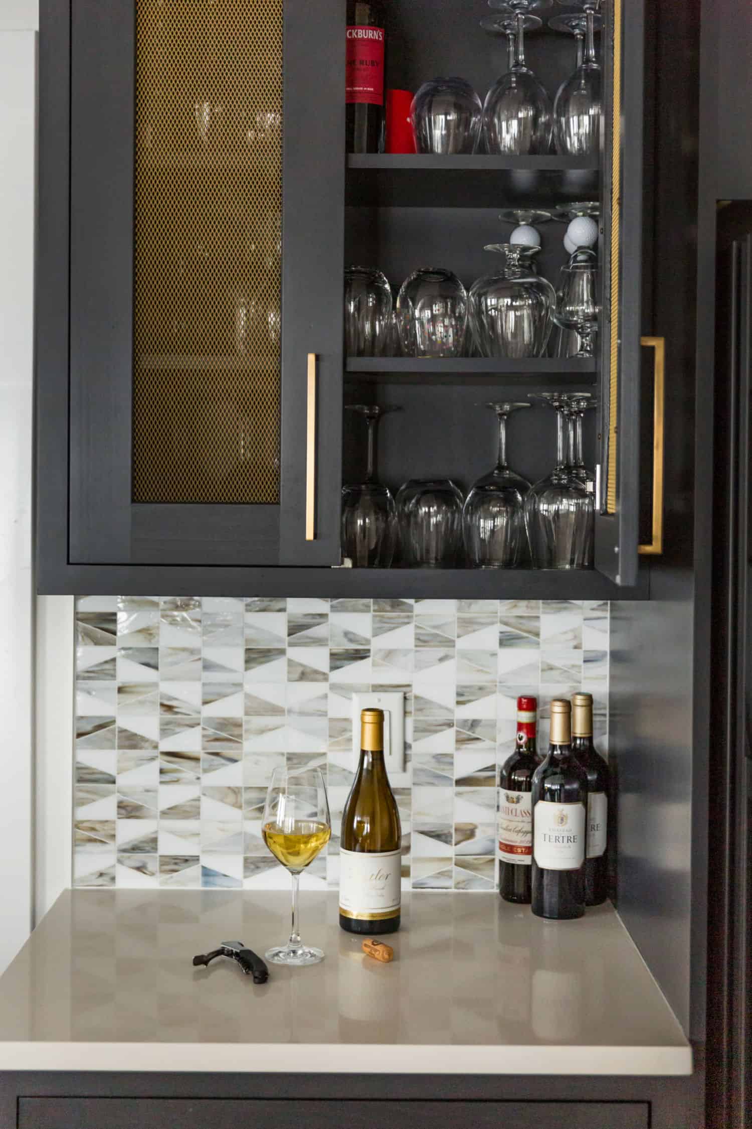 Nicholas Design Build | A black cabinet with wine glasses and a bottle of wine, perfect for a sleek remodel.