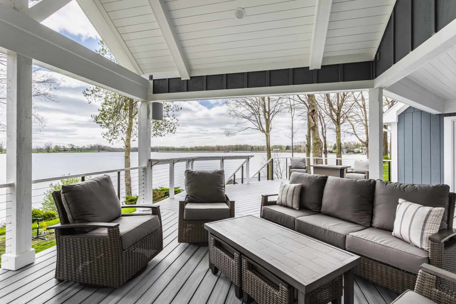 Nicholas Design Build | A remodeled deck with wicker furniture and a serene view of a lake.