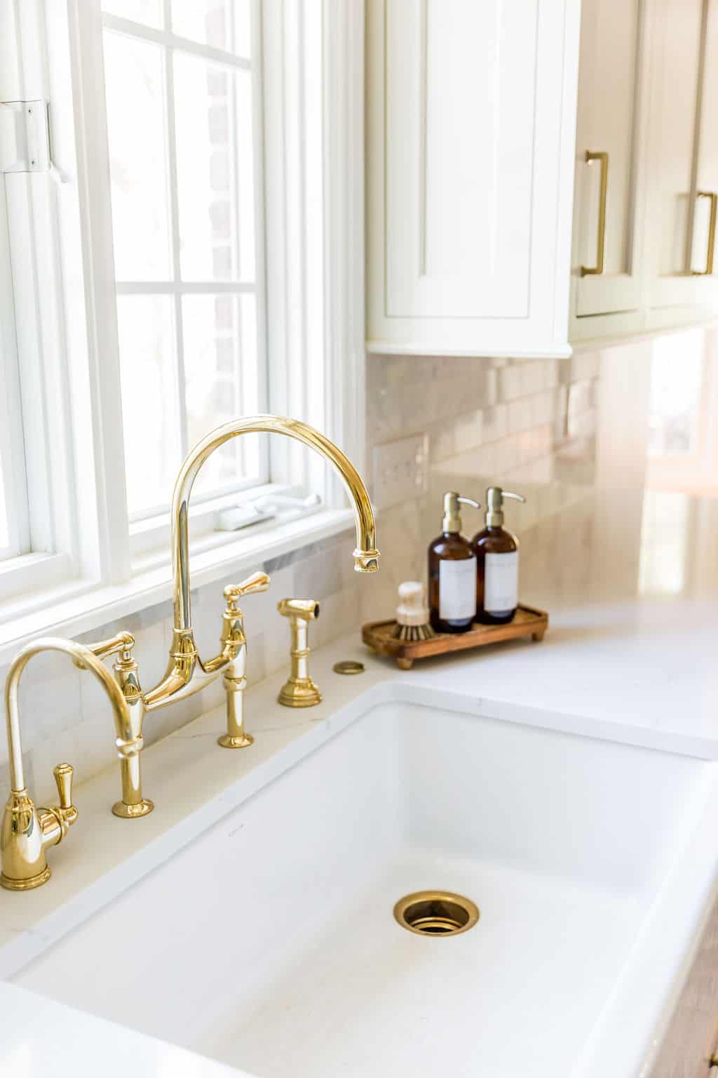 Nicholas Design Build | A white kitchen with brass faucets and a window, perfect for a remodel.