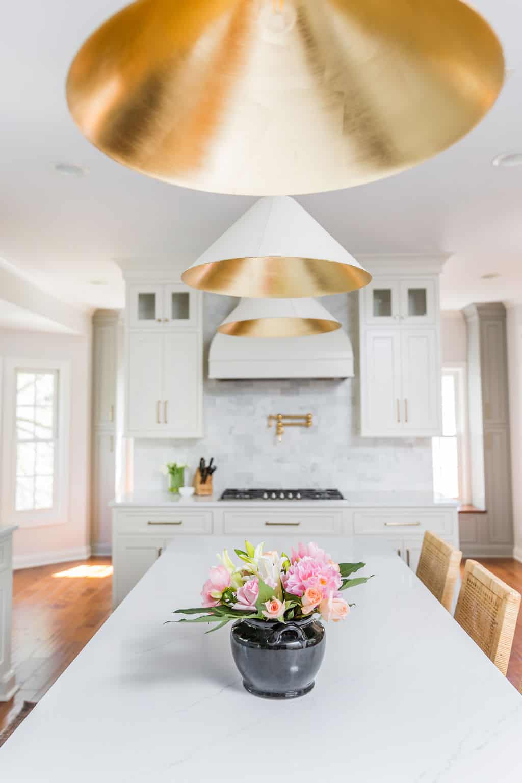 Nicholas Design Build | A remodeled kitchen with a white color scheme and a striking gold pendant hanging over the central island.