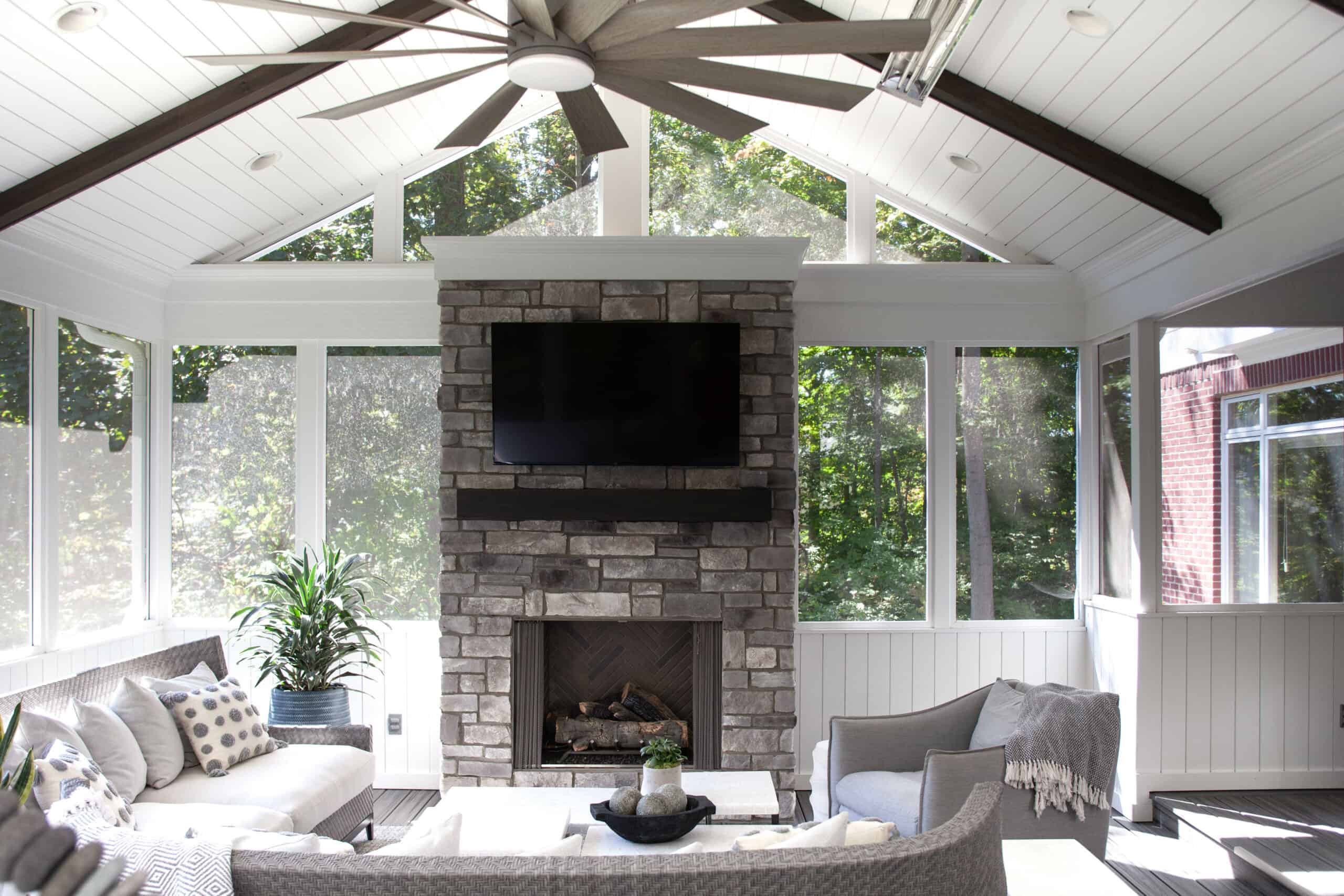 Nicholas Design Build | Remodel description: A remodeled screened-in porch featuring a cozy fireplace and a TV.