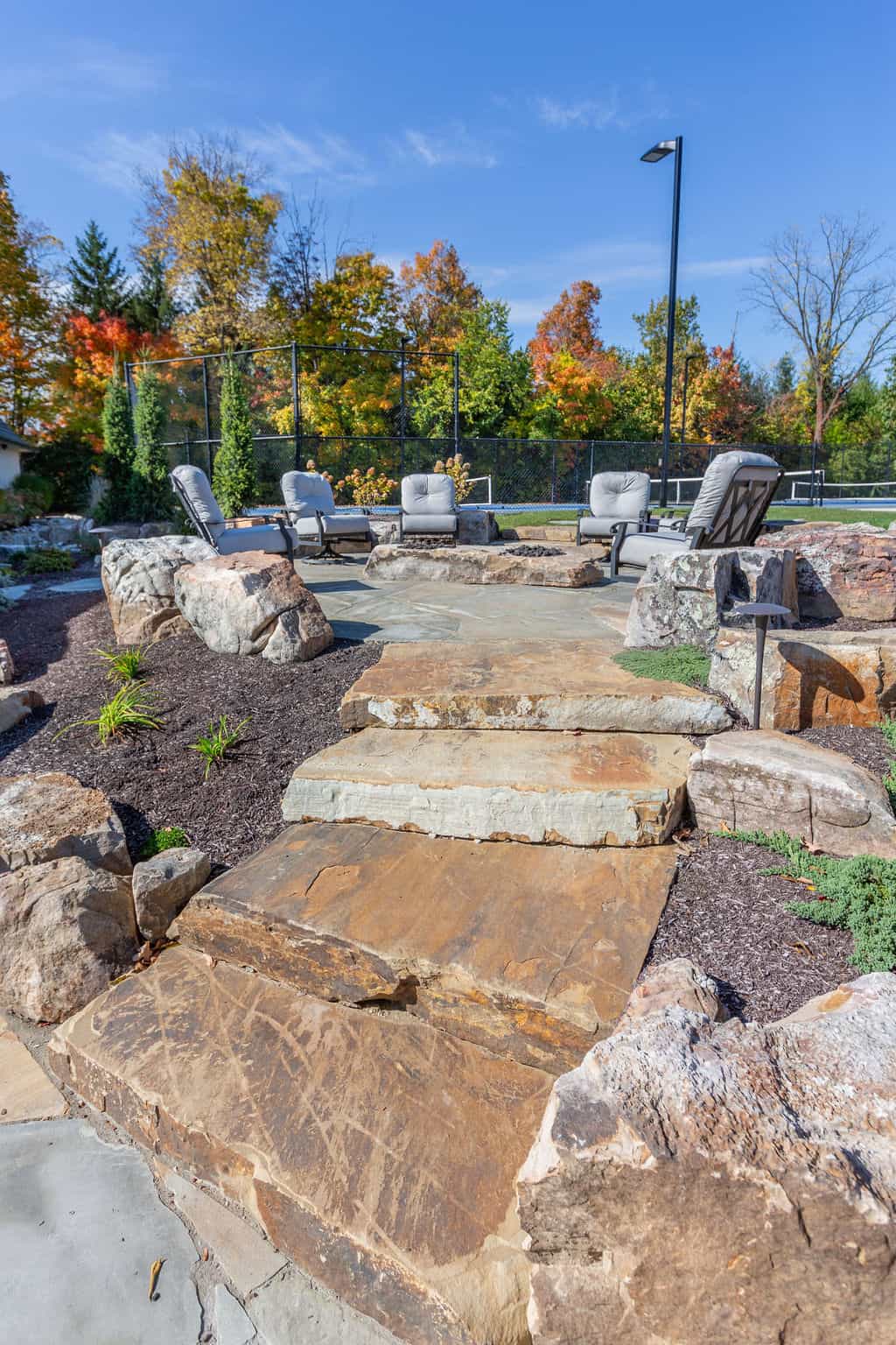 Nicholas Design Build | A stone patio with a fire pit and chairs.