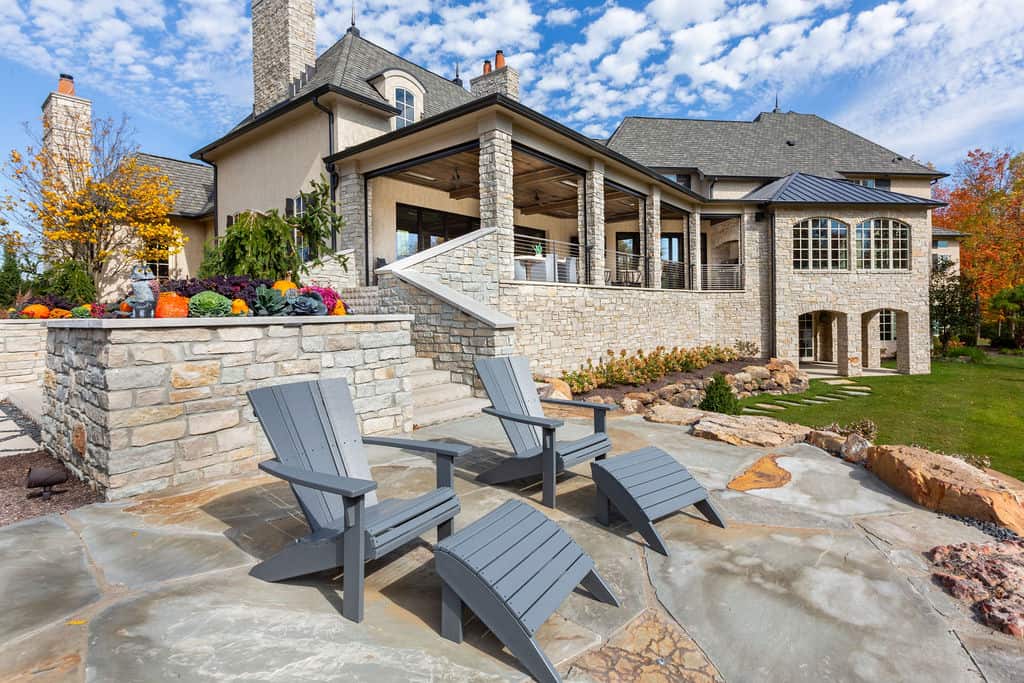 Nicholas Design Build | A stone patio with two chairs in front of a house.