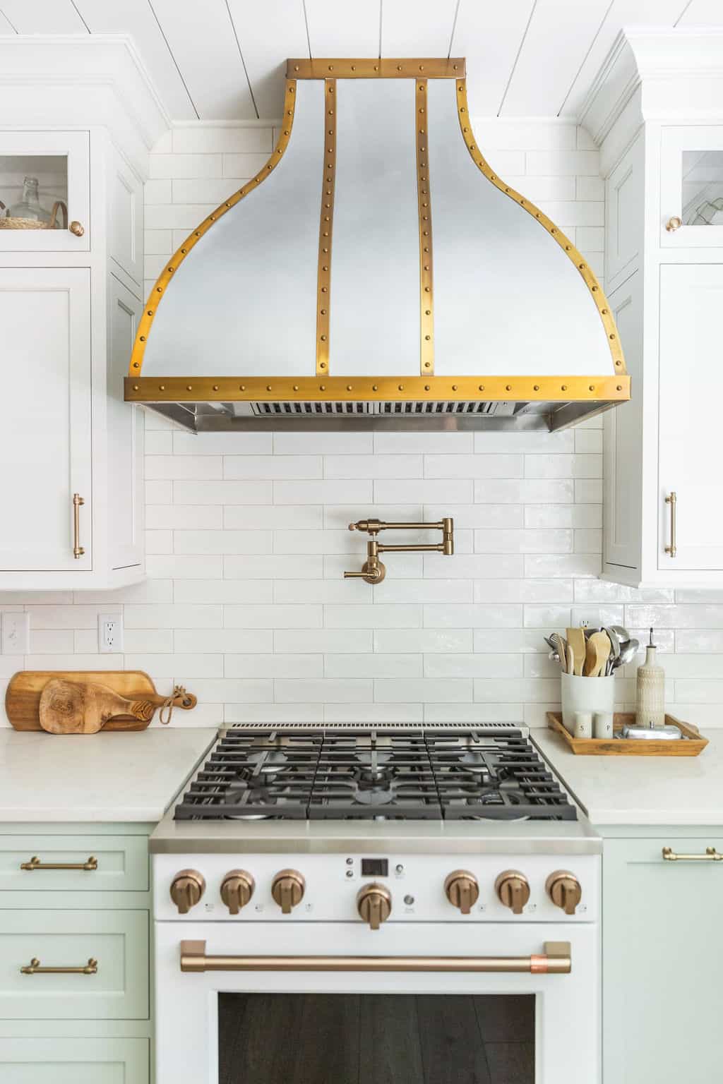 Nicholas Design Build | Elegant kitchen with a stylish brass-trimmed range hood above a professional gas stove.