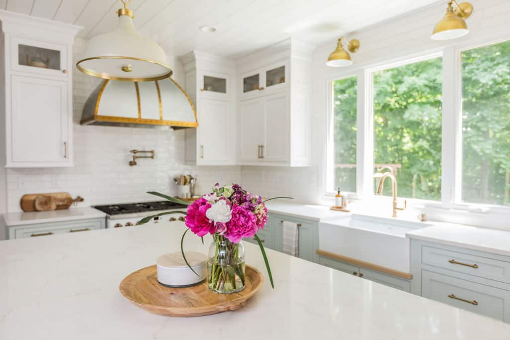 Nicholas Design Build | Bright, modern kitchen with white cabinetry and marble countertops, featuring a bouquet of pink flowers on the island.