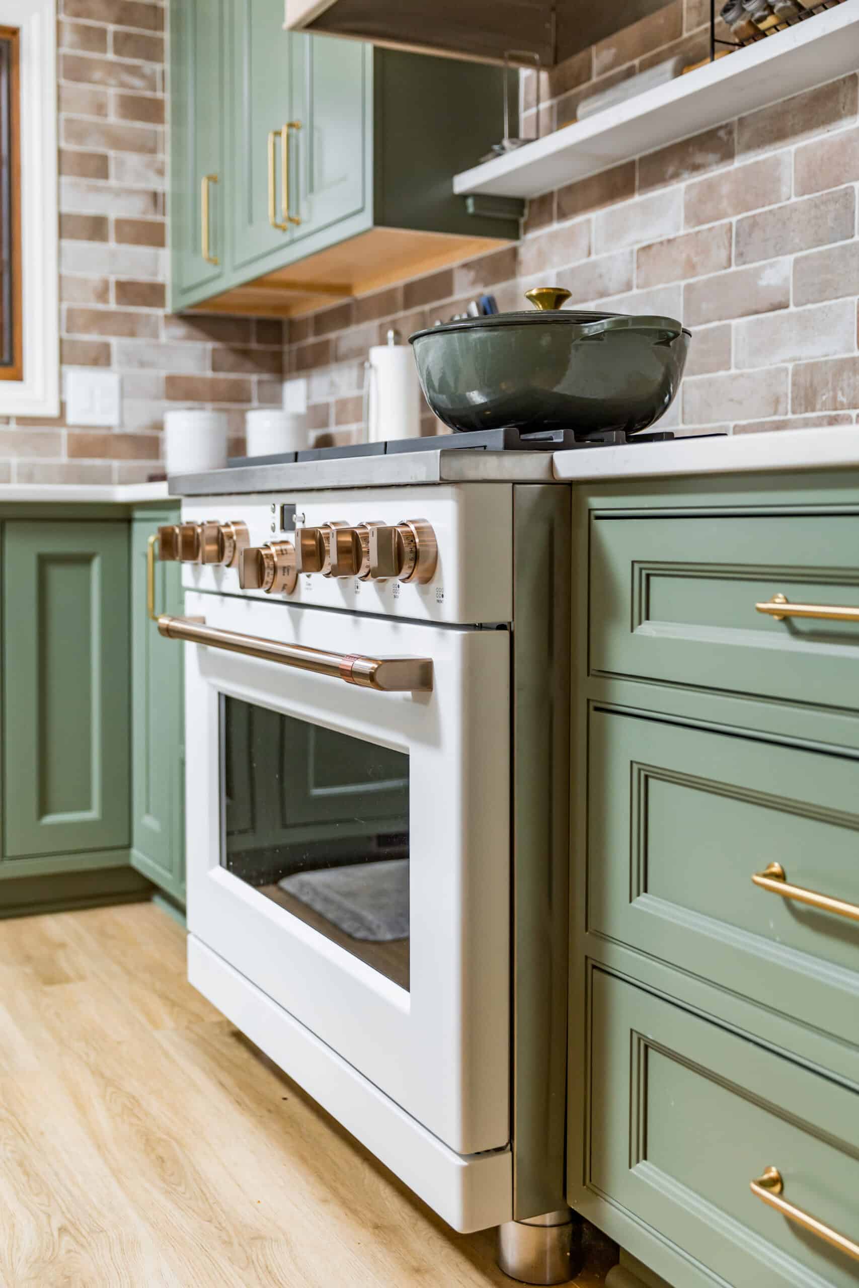 Nicholas Design Build | Modern kitchen with green cabinetry and a stainless steel stove with a frying pan on top.