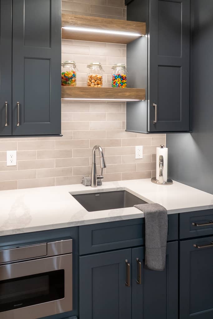 Nicholas Design Build | Modern kitchenette with dark blue cabinets, stainless steel appliances, and under-cabinet lighting.