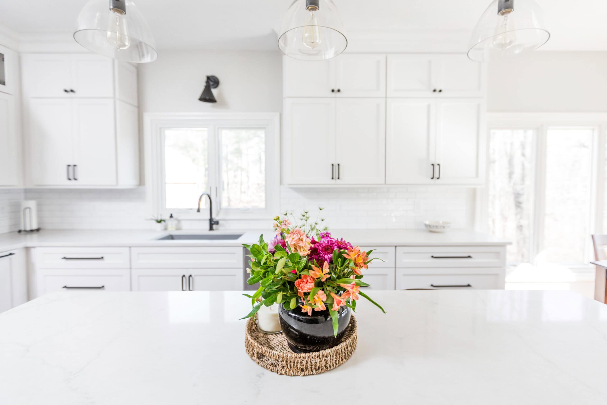 Nicholas Design Build | A bright, modern kitchen with white cabinetry and marble countertops, featuring a bouquet of colorful flowers on a central island.