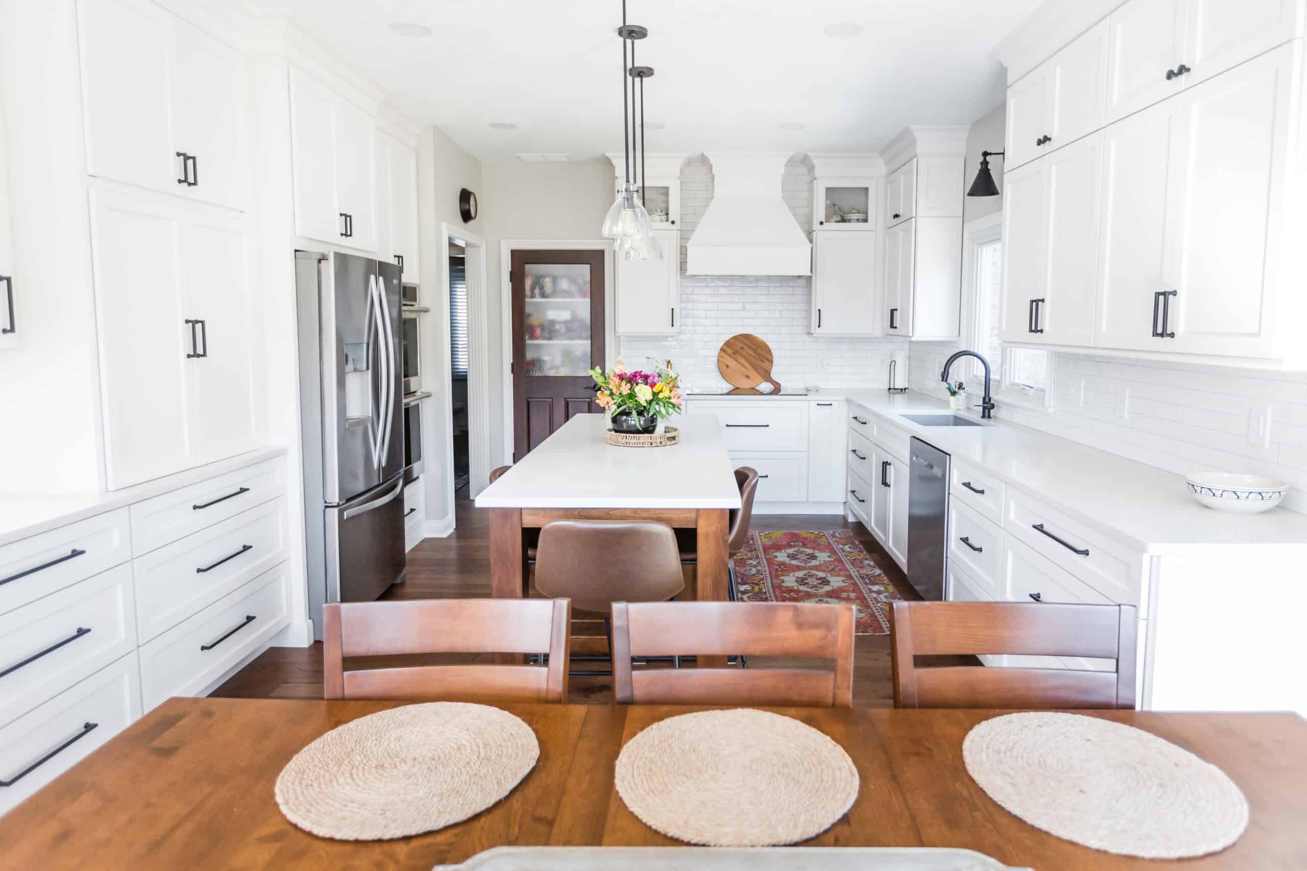 Nicholas Design Build | Bright kitchen with white cabinets, stainless steel appliances, a central island with seating, and a wooden dining table in the foreground.