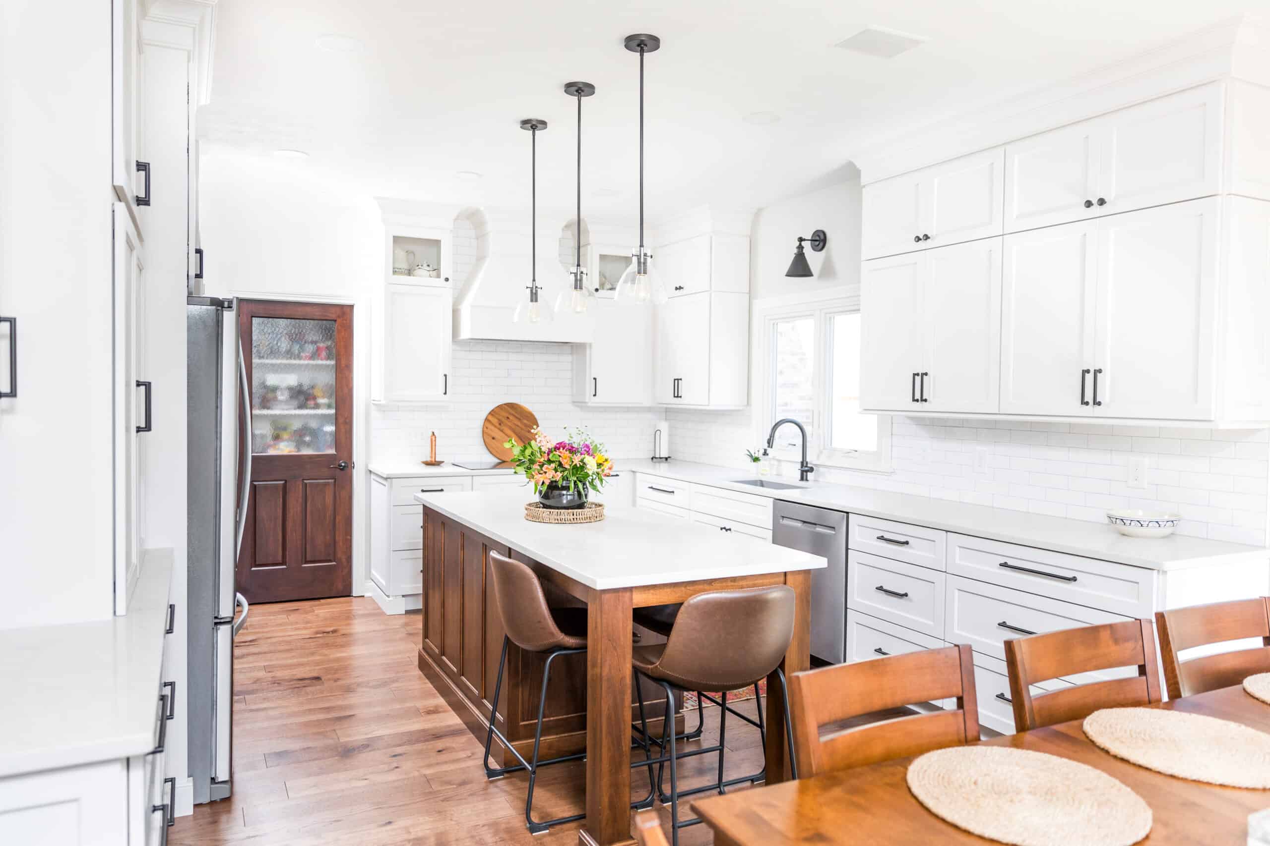 Nicholas Design Build | Modern kitchen with white cabinetry, stainless steel appliances, a central island with bar stools, and hardwood flooring.