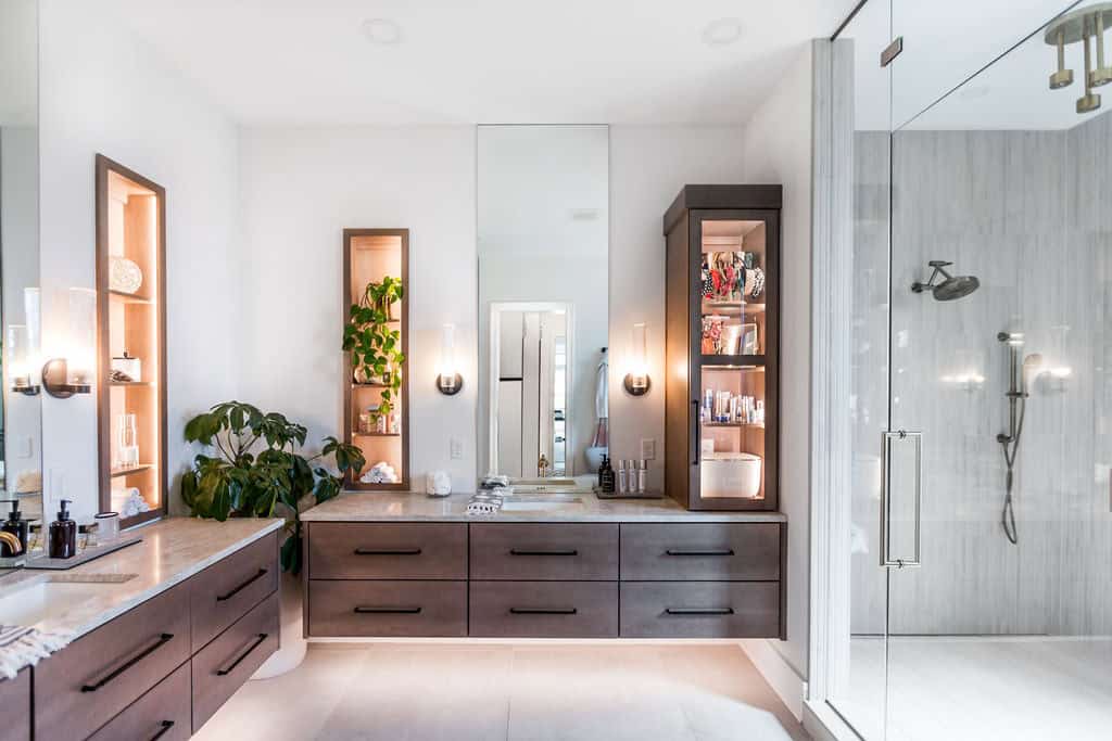 Nicholas Design Build | A modern bathroom with a large glass-enclosed shower, double sink vanity with dark wood cabinets, open shelving, and a potted plant.