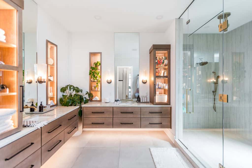 Nicholas Design Build | A modern, spacious bathroom with a large glass shower, dual sink vanity, built-in shelving, and minimalistic decor. The space is well-lit with natural light and artificial lighting.