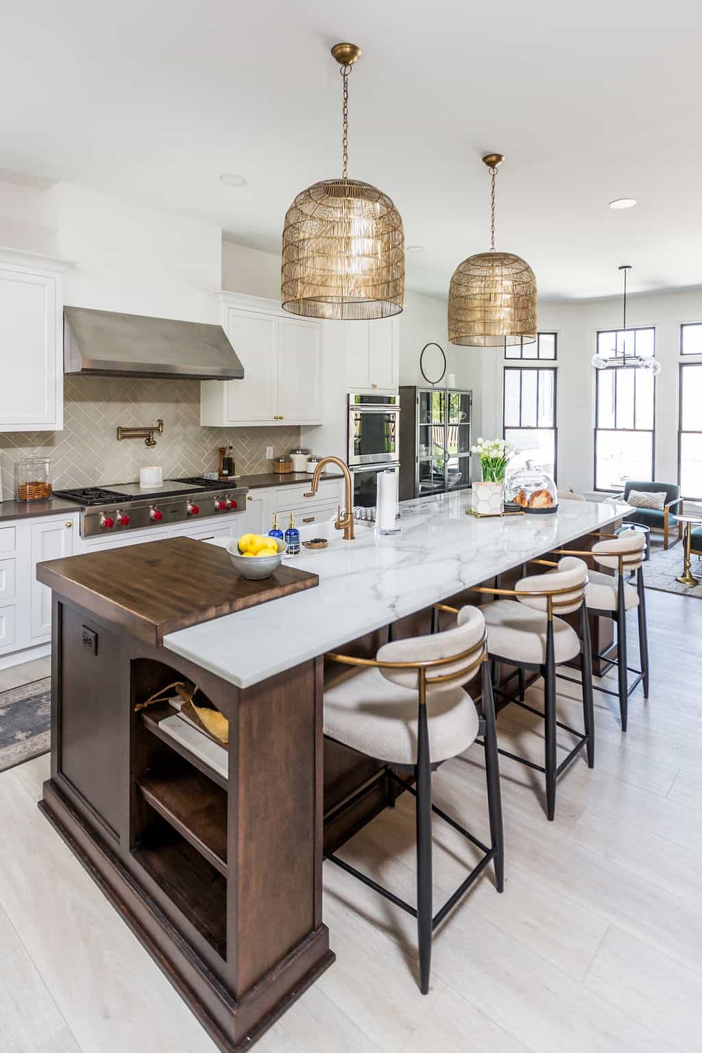 Nicholas Design Build | Modern kitchen with a large island featuring a white marble countertop, wooden base, and four bar stools. Stainless steel appliances, white cabinetry, and pendant lights complete the space.