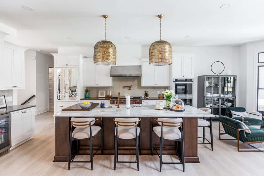 Nicholas Design Build | Modern kitchen with a central island featuring four barstools, pendant lights, white cabinetry, stainless steel appliances, and a cozy seating area.