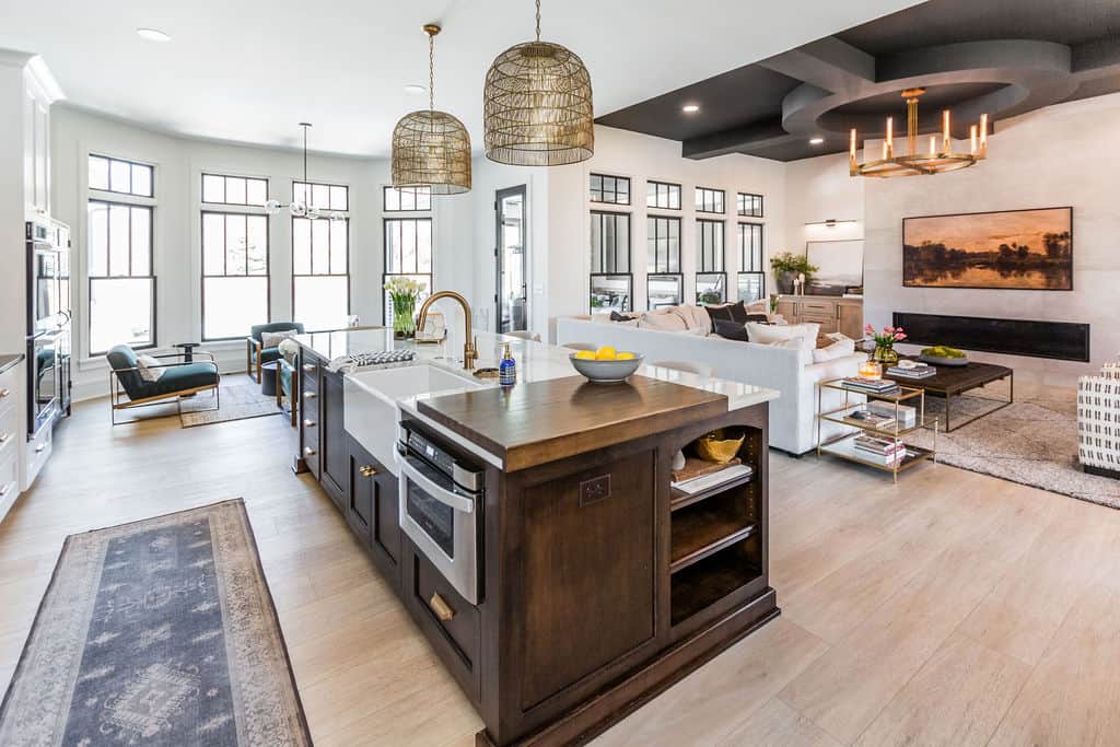 Nicholas Design Build | A modern, open-concept living area featuring a kitchen island with a sink and oven, adjacent dining and living spaces, pendant lighting, and large windows providing natural light.