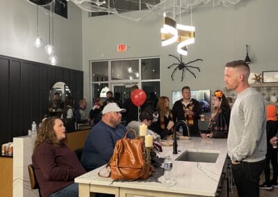 Nicholas Design Build | A group of people gather in a decorated indoor space with spider webs and balloons for a social event, engaging in conversations around a kitchen island.