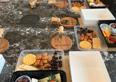 Nicholas Design Build | Plastic trays filled with assorted snacks like crackers, cheese, fruits, and sweets are arranged on a countertop with wooden coasters and empty white boxes.