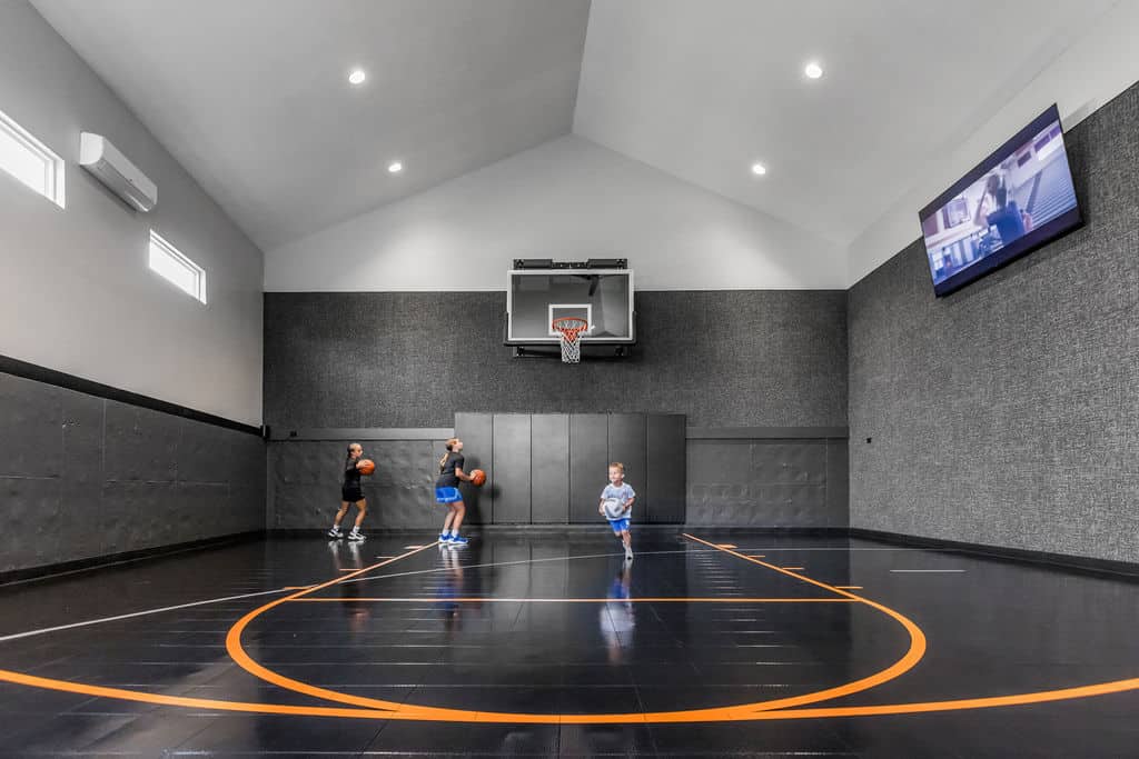 Nicholas Design Build | Two people playing basketball on an indoor court with a wall-mounted TV displaying a program above.