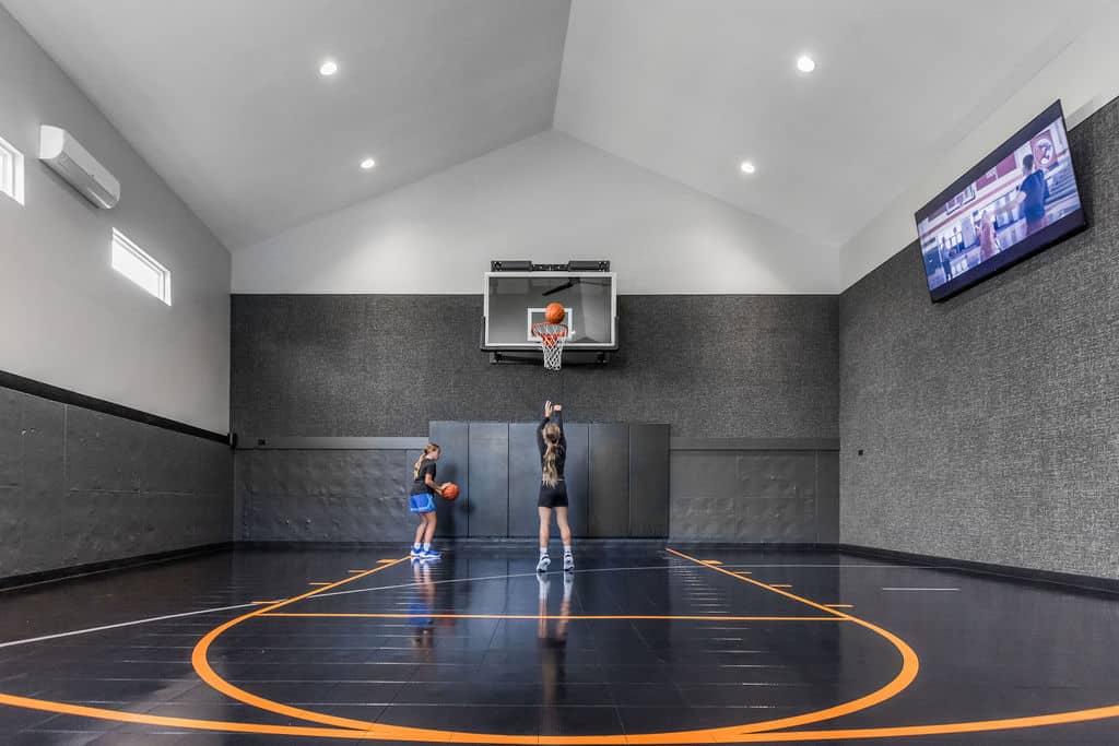 Nicholas Design Build | Two people playing basketball indoors, with one shooting and the other observing. The room has a high ceiling, and a TV is mounted on the wall above.