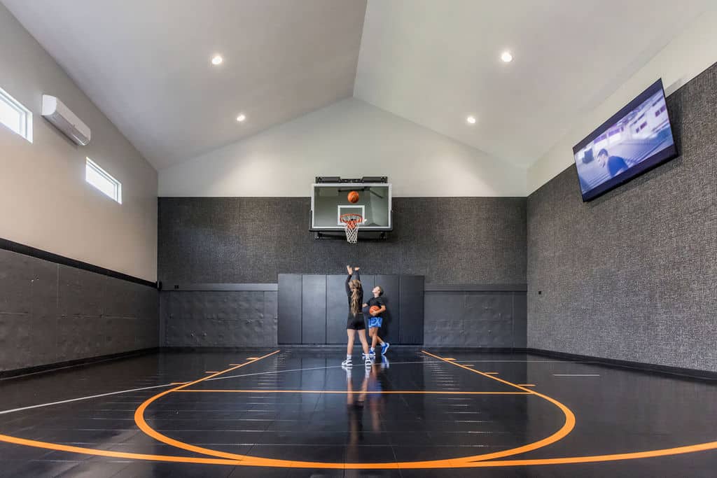 Nicholas Design Build | Two people playing basketball on an indoor court. One person is shooting while the other is defending. A television screen is mounted on the wall.