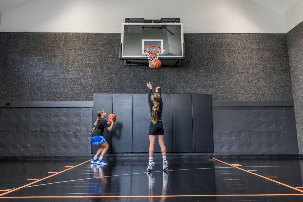 Nicholas Design Build | Two people on an indoor basketball court, one jumping to shoot the ball while the other prepares to pass.