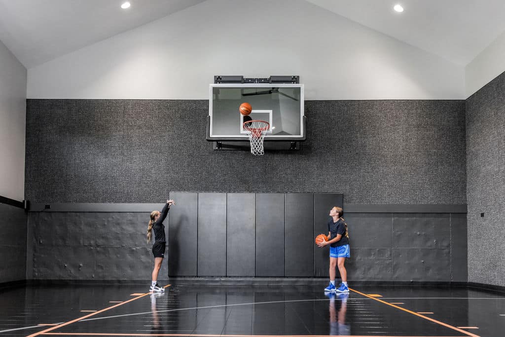 Nicholas Design Build | Two people playing basketball indoors; one is shooting, and the other is observing with a ball in hand. The court is surrounded by dark walls.