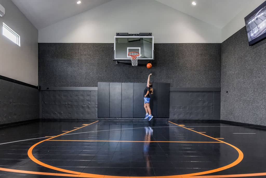 Nicholas Design Build | A person in blue sports attire jumps to shoot a basketball on an indoor court with a high ceiling and dark walls.