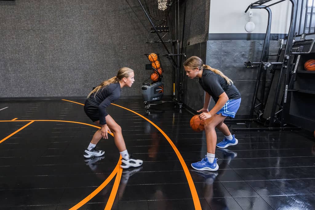 Nicholas Design Build | Two people playing one-on-one basketball on an indoor court, with one dribbling the ball and the other defending.