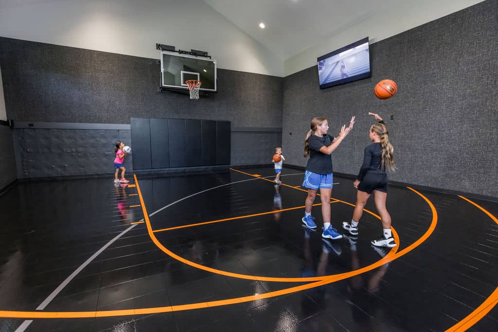 Nicholas Design Build | Children playing basketball on an indoor court with a high ceiling and a wall-mounted screen.