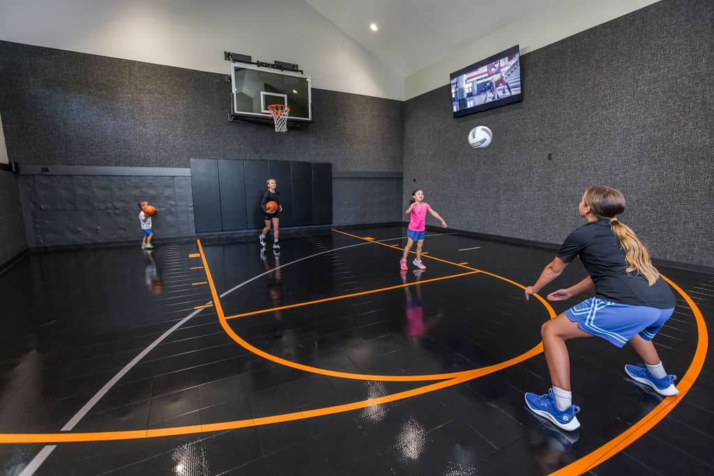 Nicholas Design Build | Four people playing basketball in an indoor court. Three are holding basketballs, and one is catching a soccer ball. A TV is mounted on the wall.